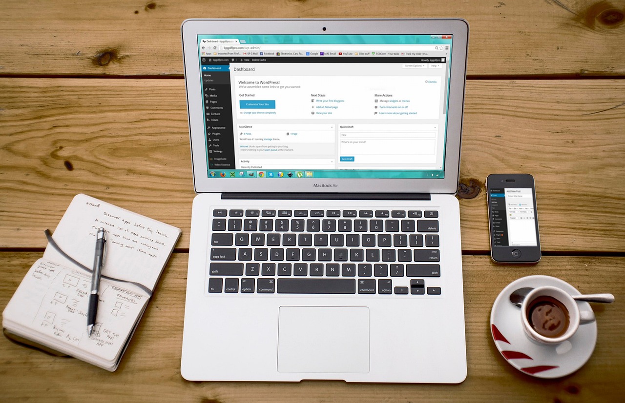 A laptop showing a WordPress dashboard beside a smartphone on a wooden desk